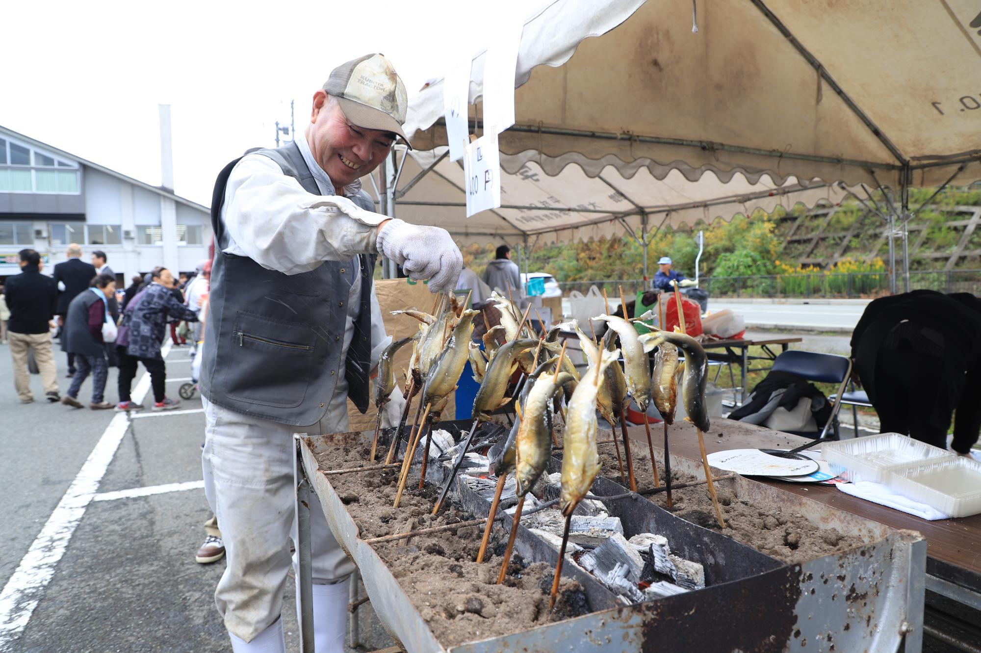 出店で販売する川魚の鮎を炭火で焼く笑顔の男性の写真