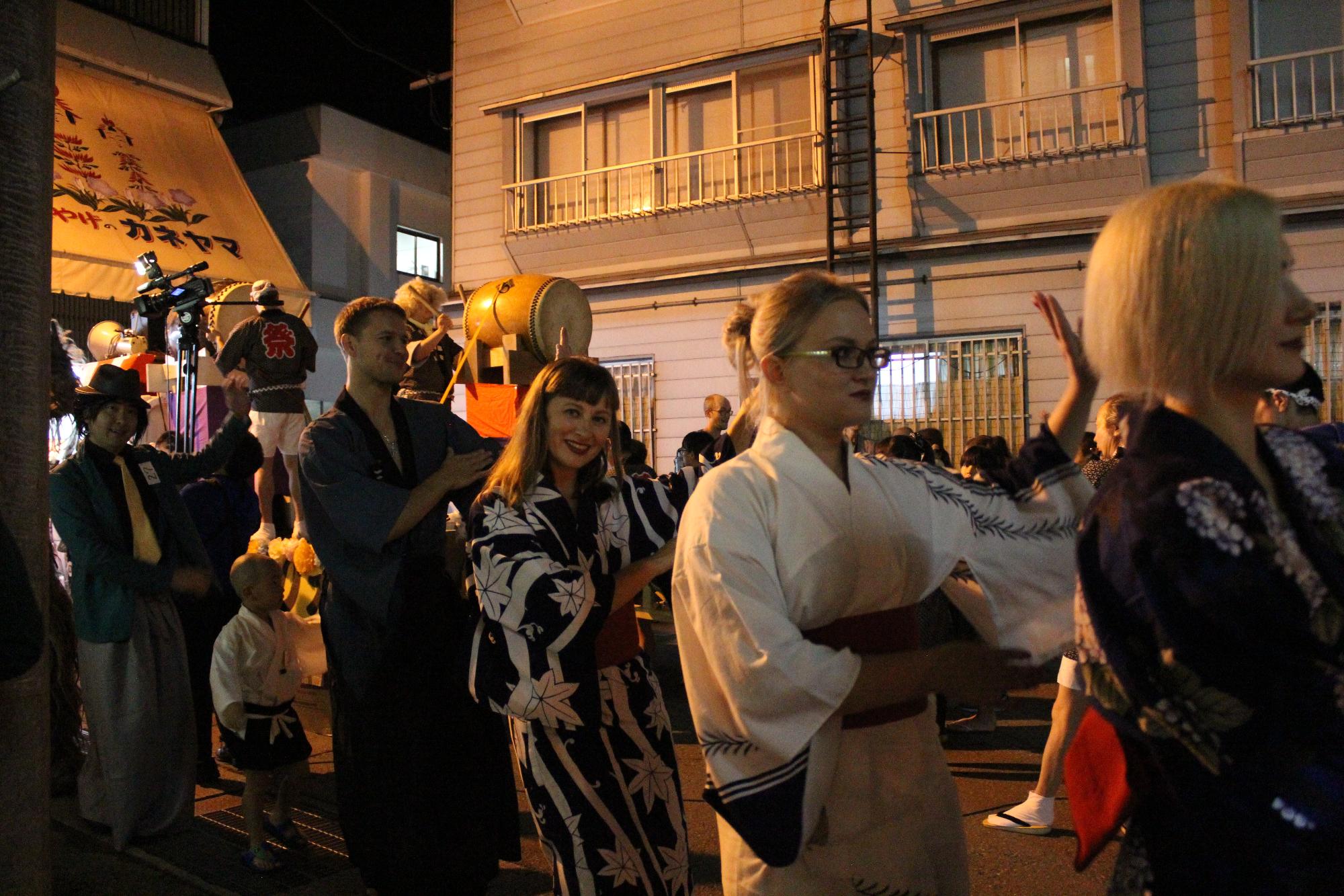 夜の温泉街に和太鼓がおかれ輪になって仮装した姿で盆踊りを踊る人々の写真